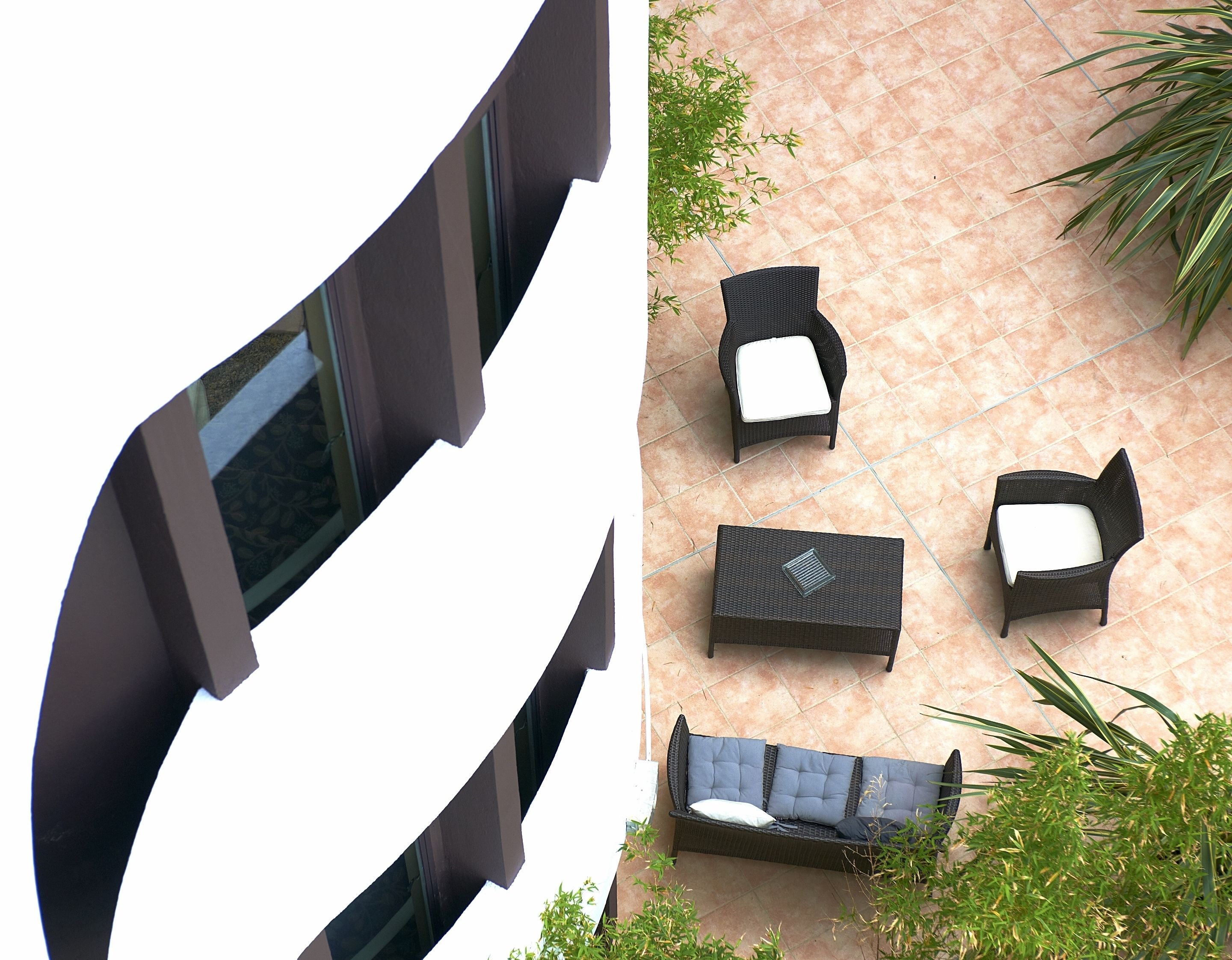 A modern outdoor seating area with a sofa and two chairs, surrounded by potted plants.