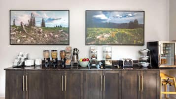 Una encimera de cocina con varios electrodomésticos, una cafetera, un frutero y un molinillo de café.