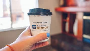 En hånd holder en kaffekop med låg, et synligt logo og tekst, der angiver et loyalitetsprogram.