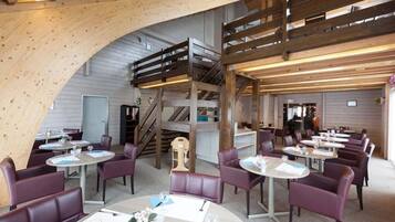A restaurant with round tables and purple chairs, a wooden staircase, and a high ceiling with exposed beams.