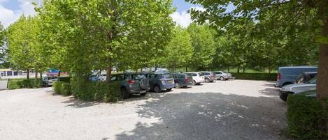 Un estacionamiento con varios coches aparcados bajo árboles.