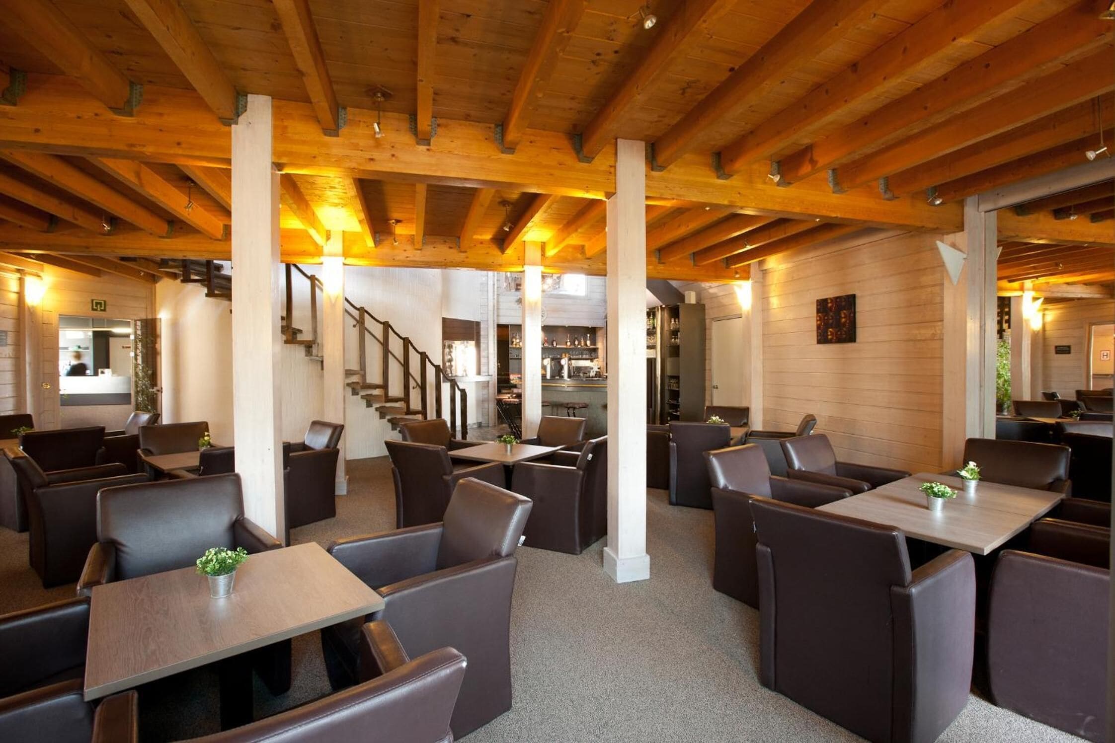 A restaurant with wooden beams, brown leather booths, and a staircase leading to the kitchen.