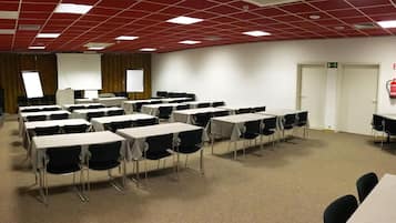 A conference room with multiple tables and chairs, white walls, and a red ceiling with grid patterns.