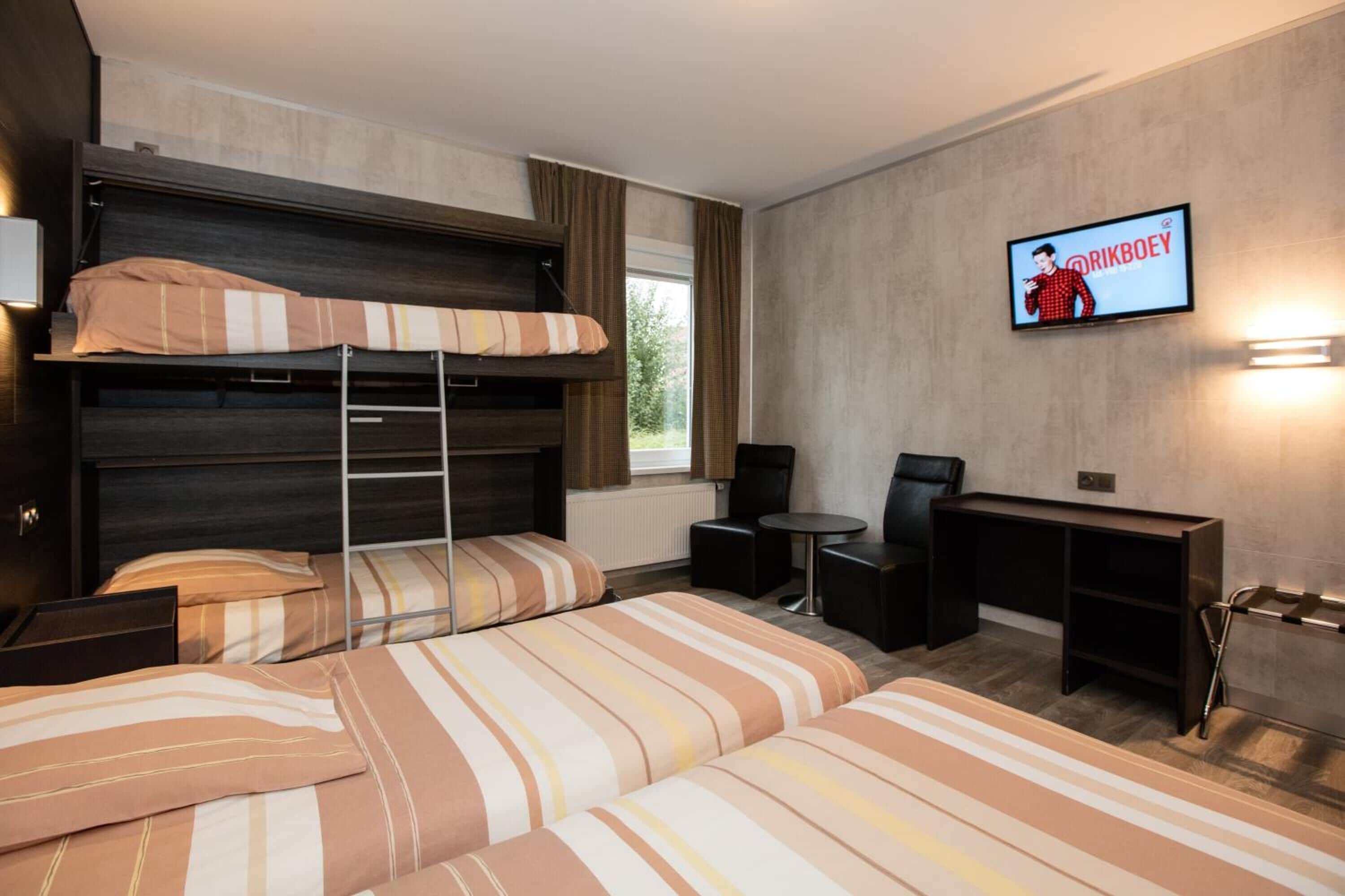 Een hotelkamer met een stapelbed, een bureau, een stoel en een televisie aan de muur.