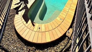 Une piscine au design incurvé, entourée d’une terrasse en briques et de rampes en métal.
