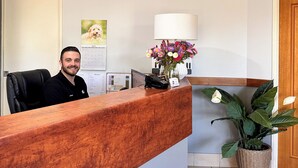 Un comptoir d’accueil en bois, une plante en pot, une lampe fixée au mur et un tableau encadré.