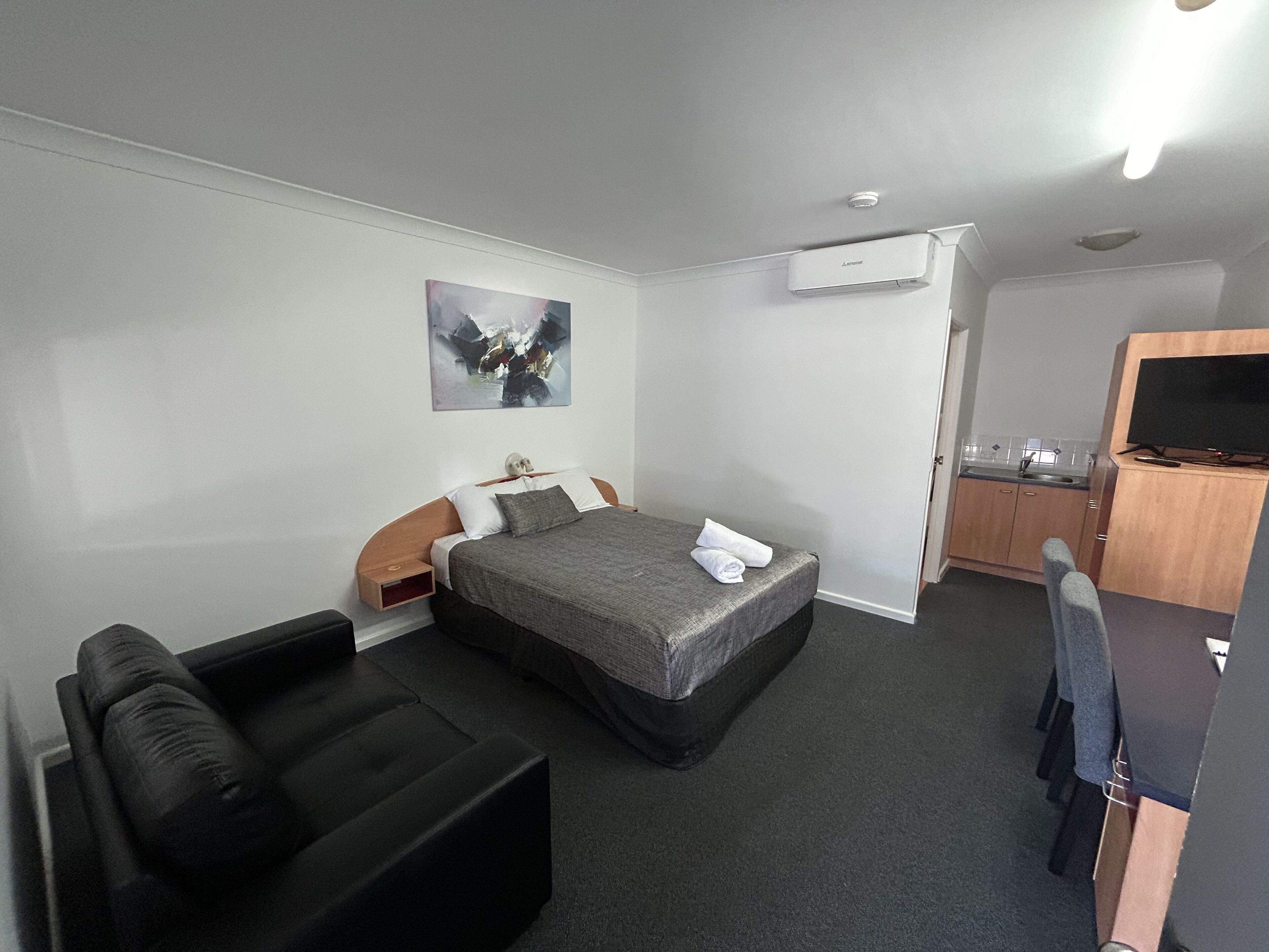Et hotelværelse med en seng, en lille sofa, et skrivebord med fjernsyn og et tekøkken.