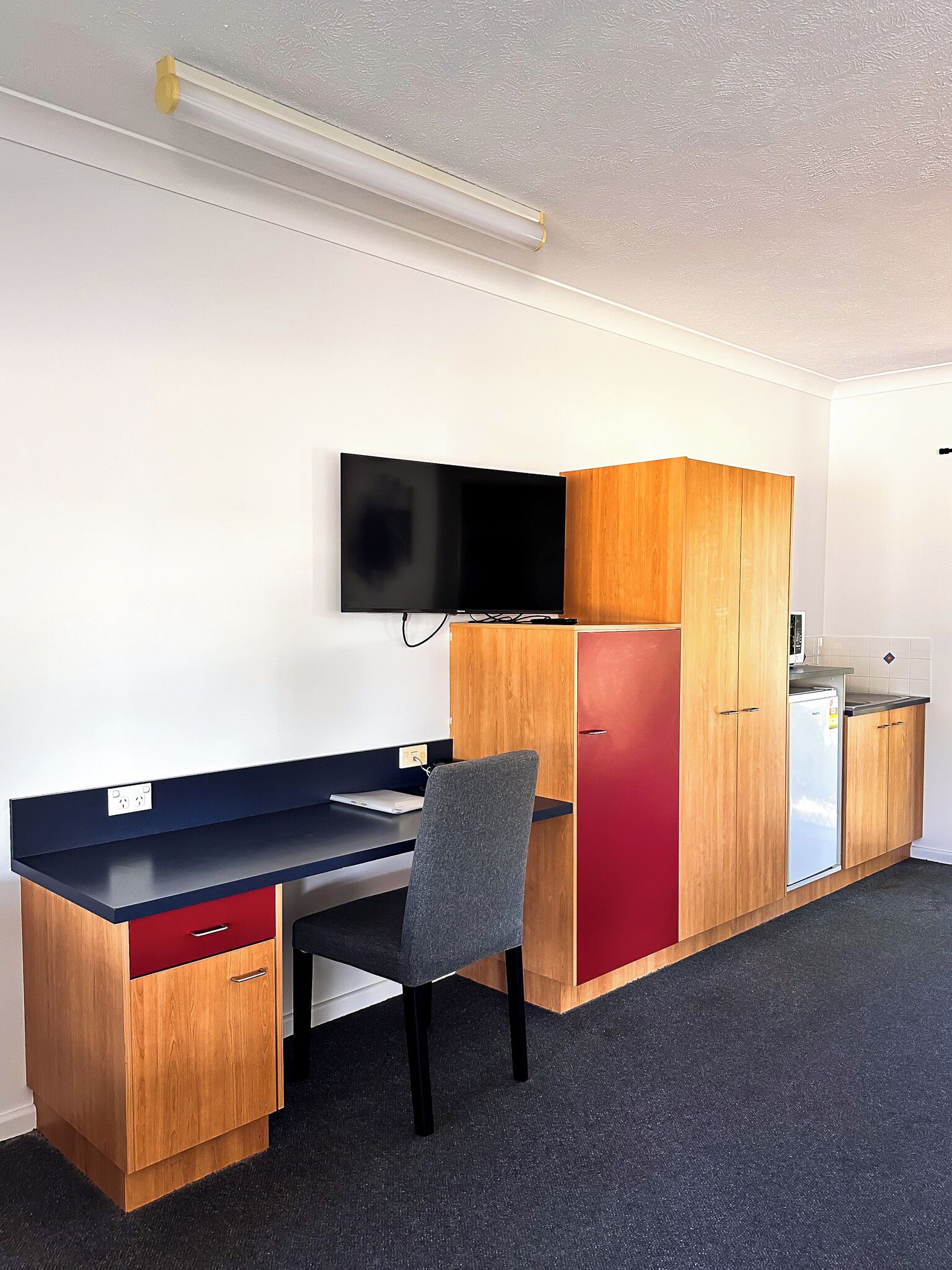 Habitación compacta con escritorio, silla, televisor y armarios de madera.