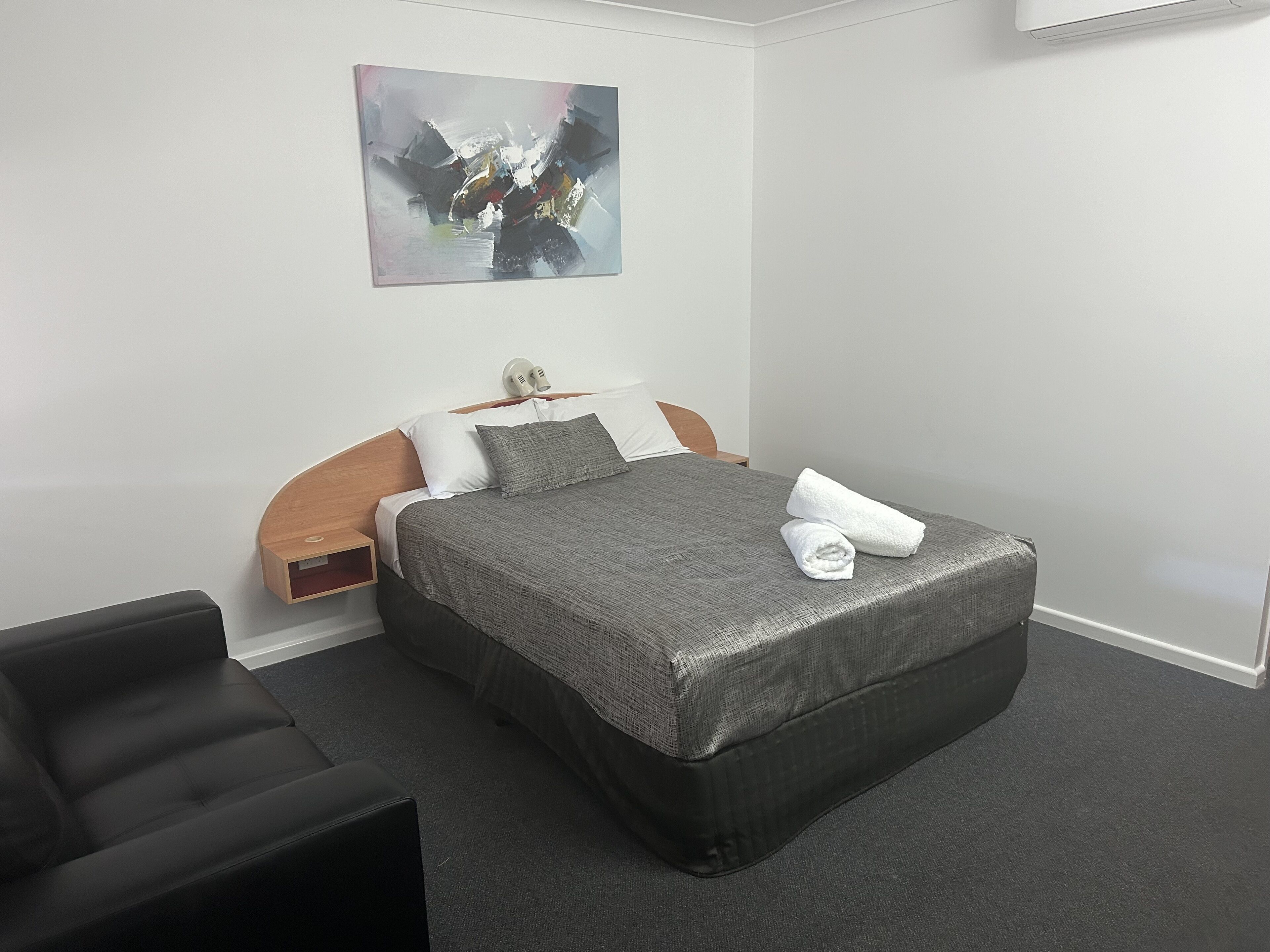 Habitación de hotel con cama, una silla, un cuadro en la pared y una mesita de noche.