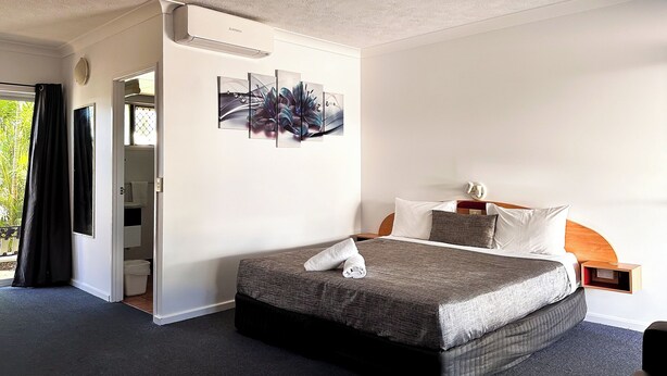 Une chambre d’hôtel comprenant un lit, une table de chevet, un climatiseur fixé au mur et une porte donnant sur un balcon.