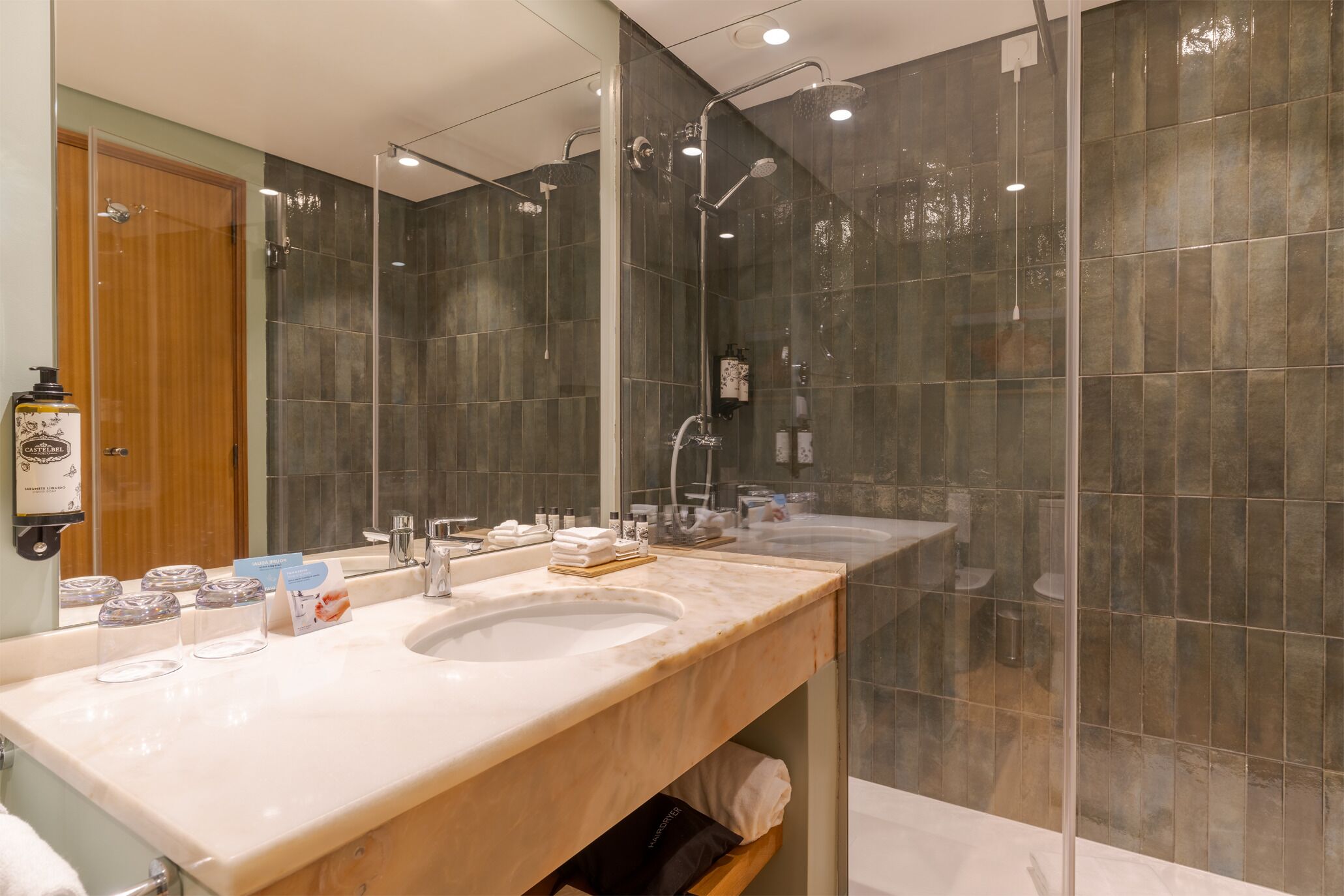 Un baño moderno con dos lavamanos, un espejo grande y cabina de ducha con paredes de vidrio.