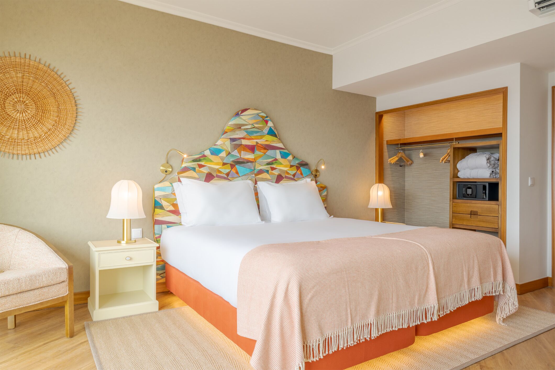 A bedroom with a bed, two bedside tables with lamps, a wardrobe, and a decorative wall hanging.