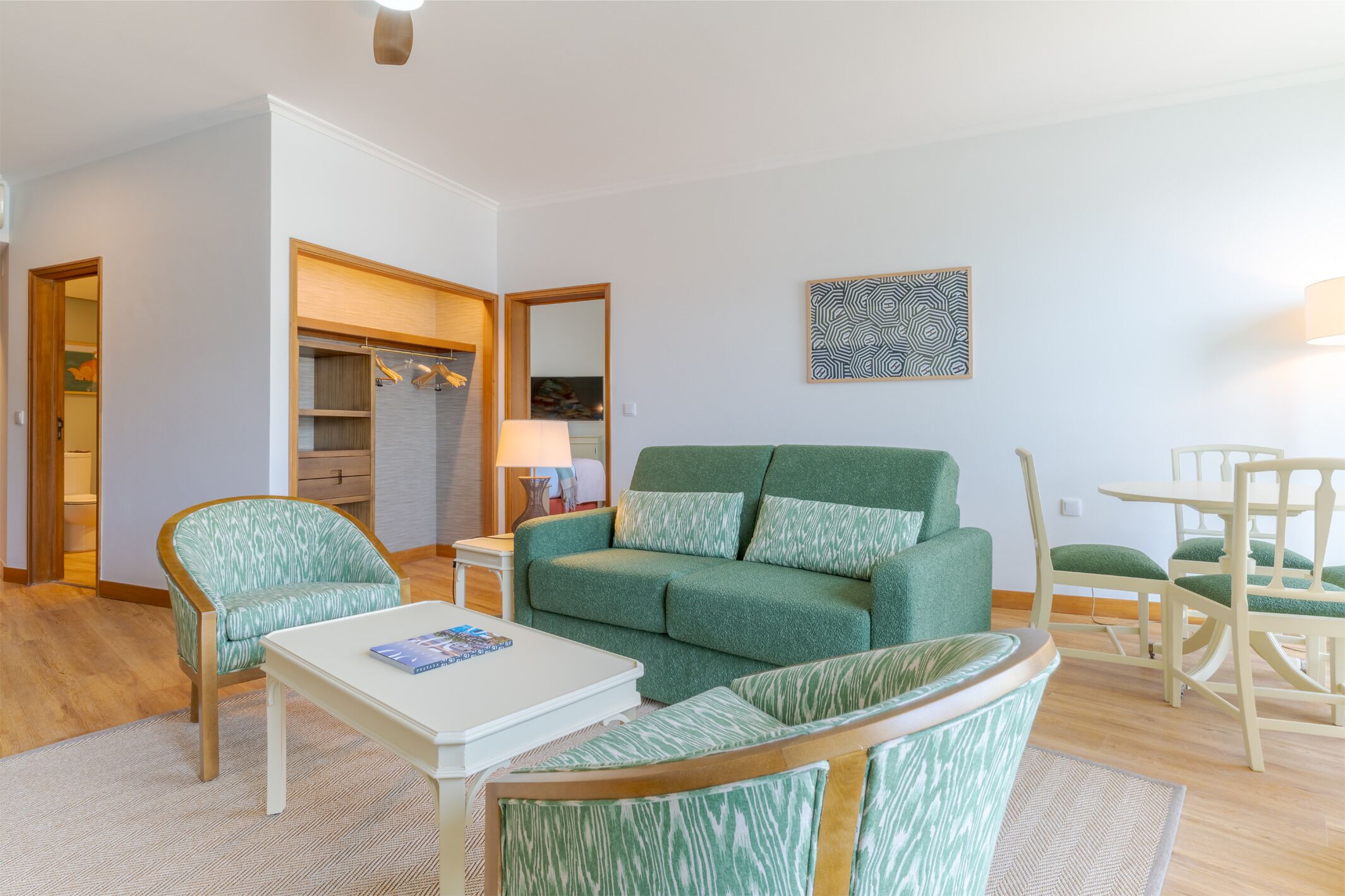 Een woonkamer met een groene bank, een bijpassende fauteuil, een kleine witte tafel en een eethoek met een houten tafel en stoelen.
