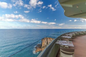 A deck with tables and chairs overlooking the ocean with a rocky coastline. - Pestana Vila Lido Madeira Ocean Hotel (Funchal)