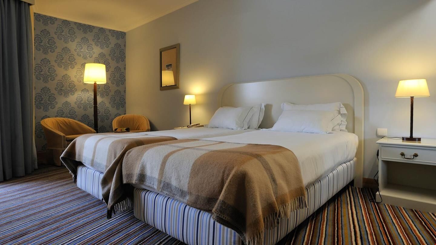 A hotel room with a large bed, two bedside tables, a chair, and a patterned carpet.