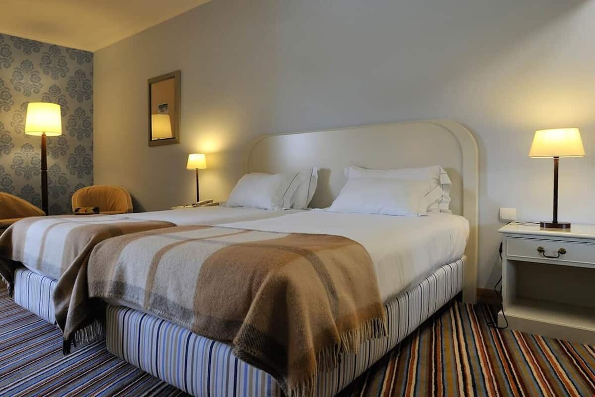 A hotel room with a large bed, two bedside tables, a chair, and a patterned carpet.