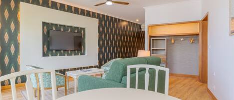 A living room with a TV mounted on the wall, a ceiling fan, and a green sofa.