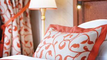 A neatly made bed with a patterned pillow and red accents, a bedside lamp, and curtains with a red and white pattern.