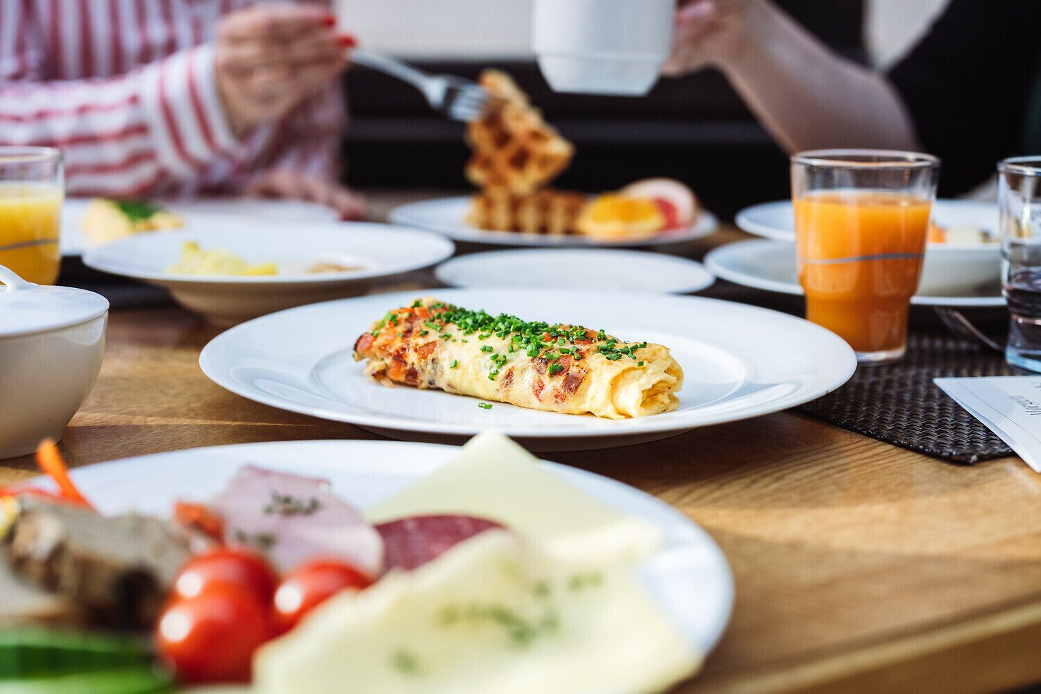 A breakfast setting with plates of food, including a rolled dish garnished with herbs, and glasses of orange juice.
