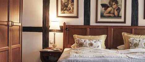 A bedroom with a large bed, a nightstand with a lamp, and two framed pictures on the wall.