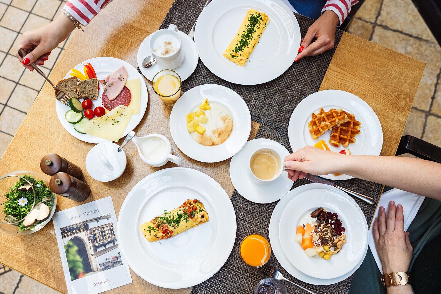 A breakfast setting with various dishes, including waffles, omelets, and a ham and cheese plate, on a wooden table.