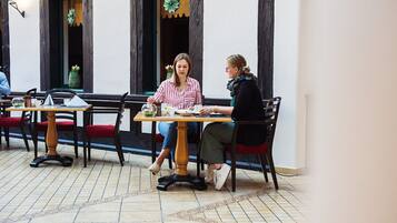 An indoor dining area with wooden tables and chairs, a tiled floor, and a window with decorative elements.