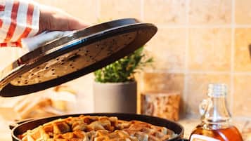 A hand lifting a lid off a pan of food, with a bottle of sauce and a card on the counter.