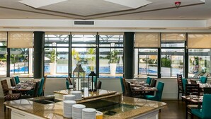 Een restaurant met een centraal eiland, meerdere eettafels en stoelen. Grote ramen bieden uitzicht op het omliggende landschap.