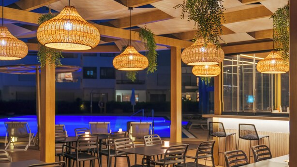 Een terras met een eethoek, rieten hanglampen, houten tafels en stoelen.