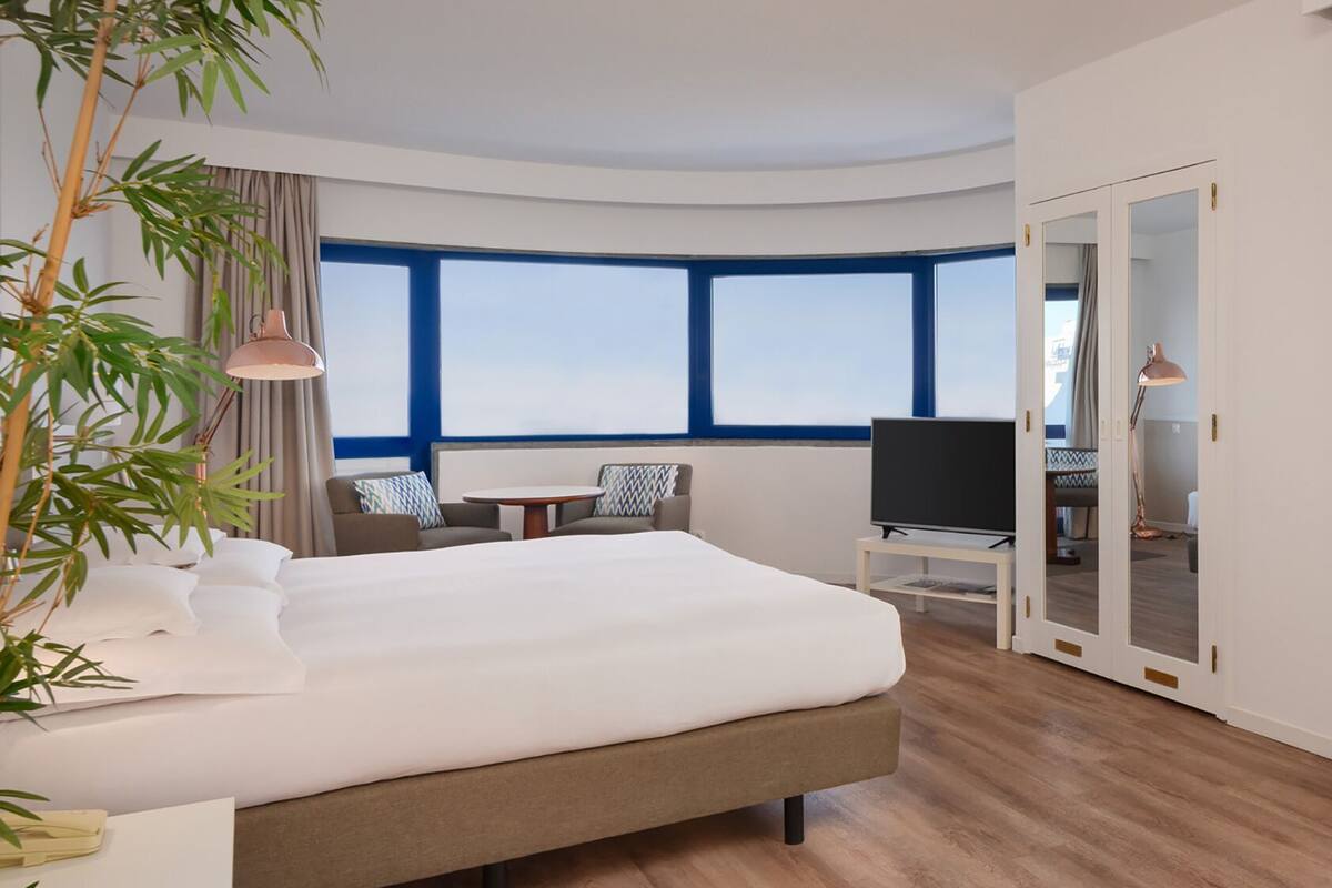 Une chambre d’hôtel moderne dotée d’un grand lit, d’une télévision, d’un bureau et offrant une vue sur la ville grâce à de grandes fenêtres.