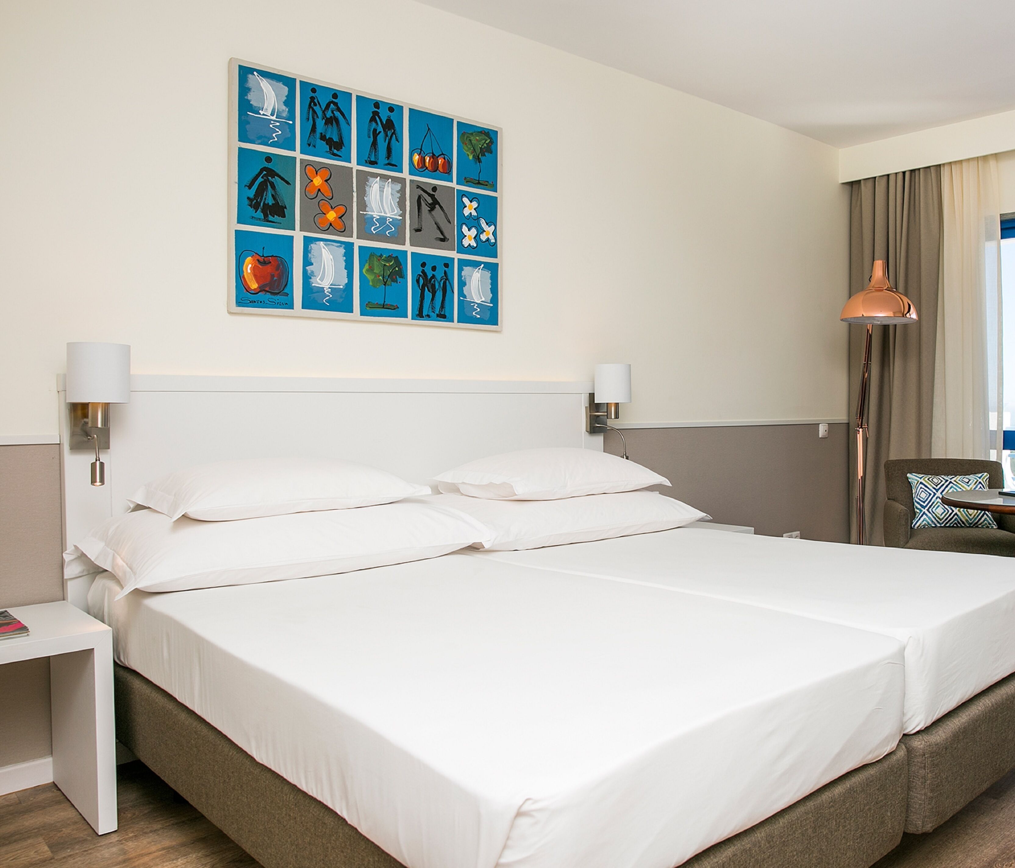 A hotel room with a large bed, two bedside lamps, a wall art piece, a nightstand, a chair, and a window with curtains.