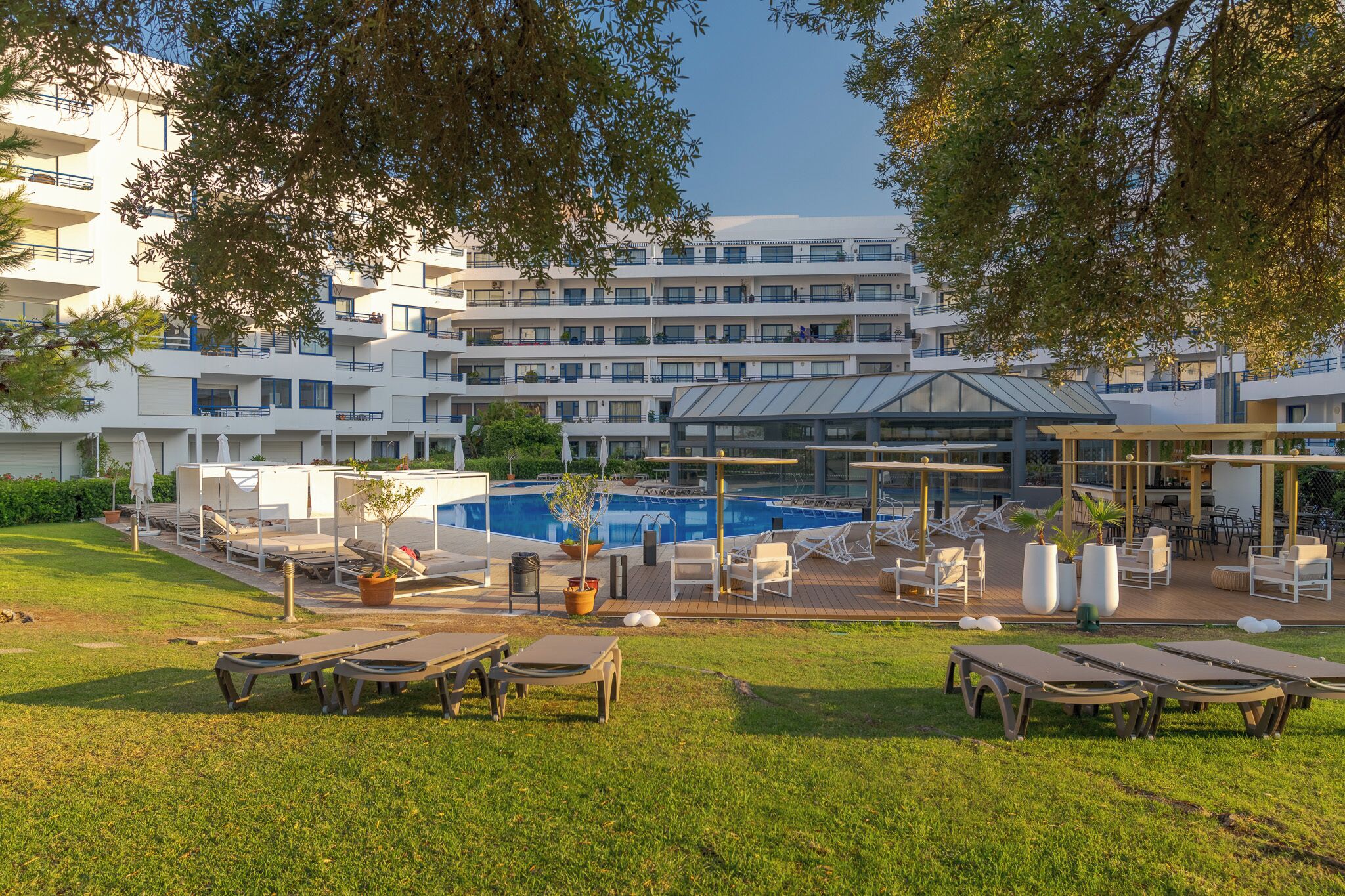 Un hotel con piscina, mobiliario exterior y un patio cubierto.