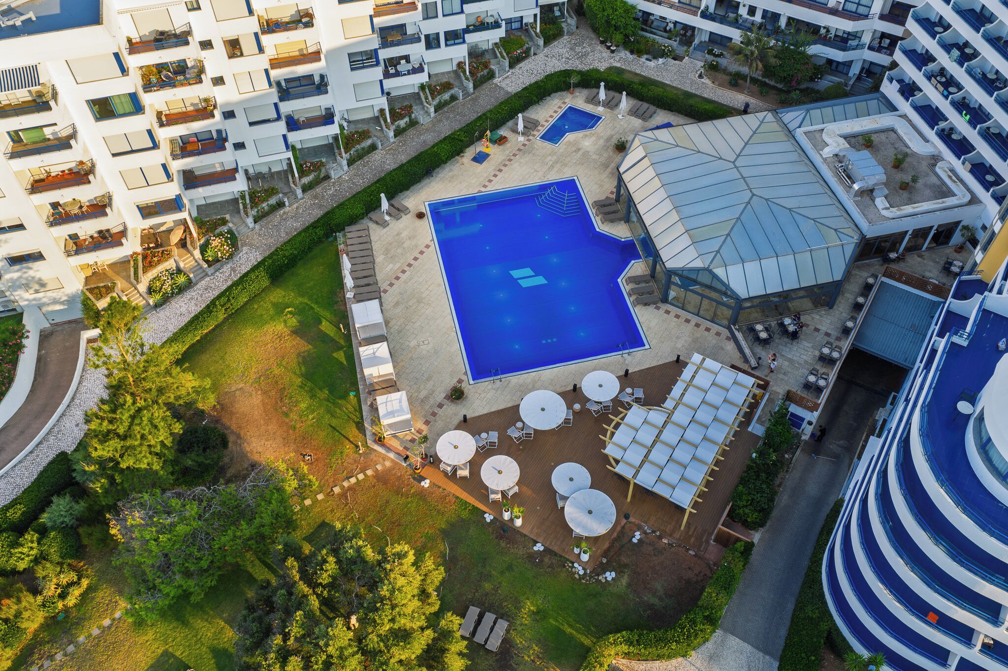 Eine Vogelperspektive auf ein Hotel mit einem zentralen Swimmingpool, Außenbereich-Sitzgelegenheiten und mehreren Balkonen.