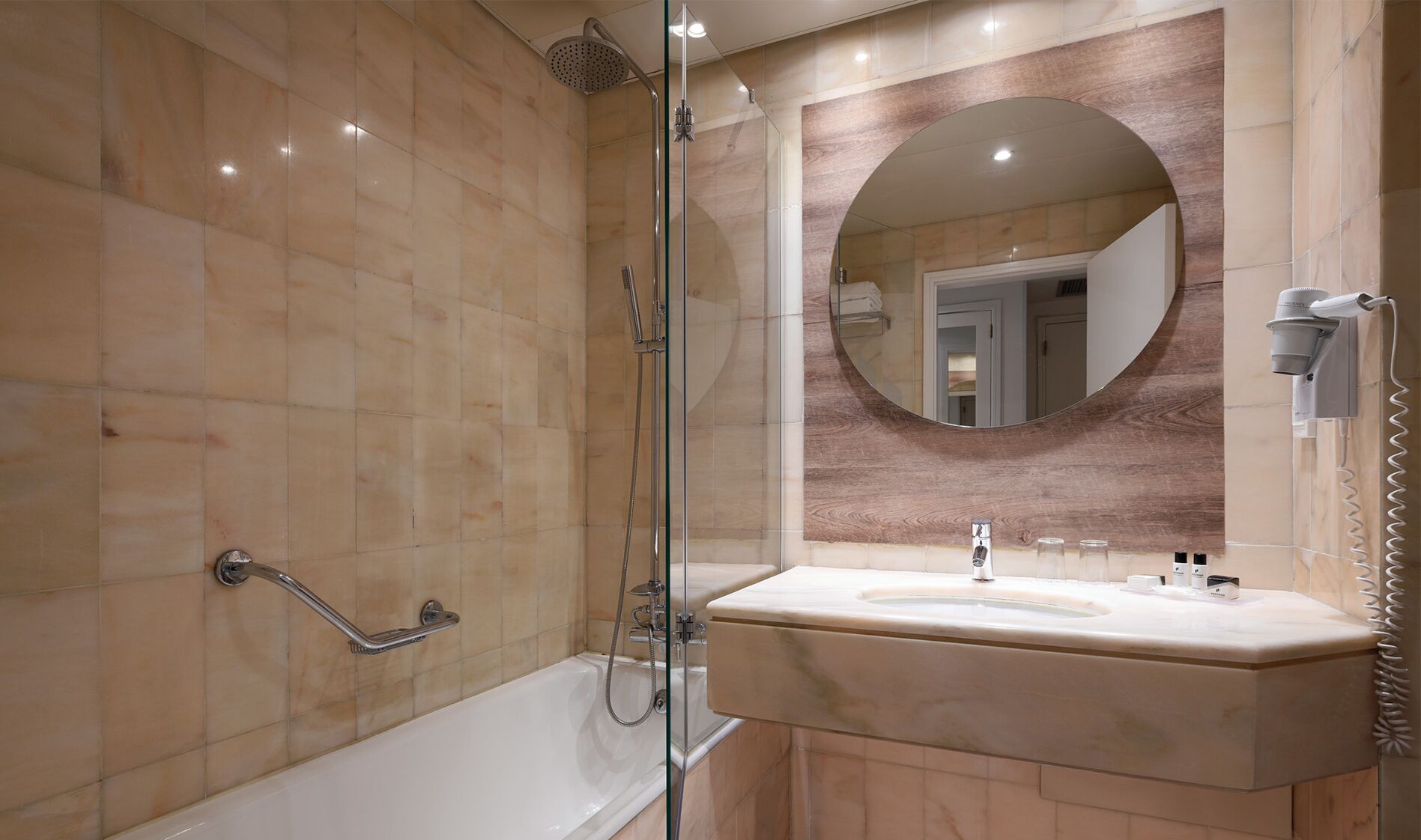 Un baño moderno con ducha envuelta en cristal, tocador con lavabo y espejo redondo.