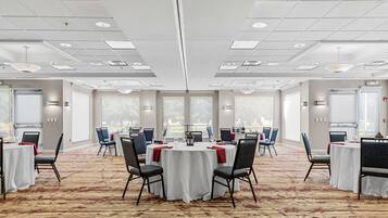 Un salón de conferencias con mesas redondas, sillas y piso alfombrado.