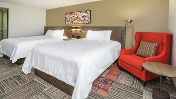 Habitación de hotel con dos camas, un sillón rojo, una mesita y una lámpara de pared.