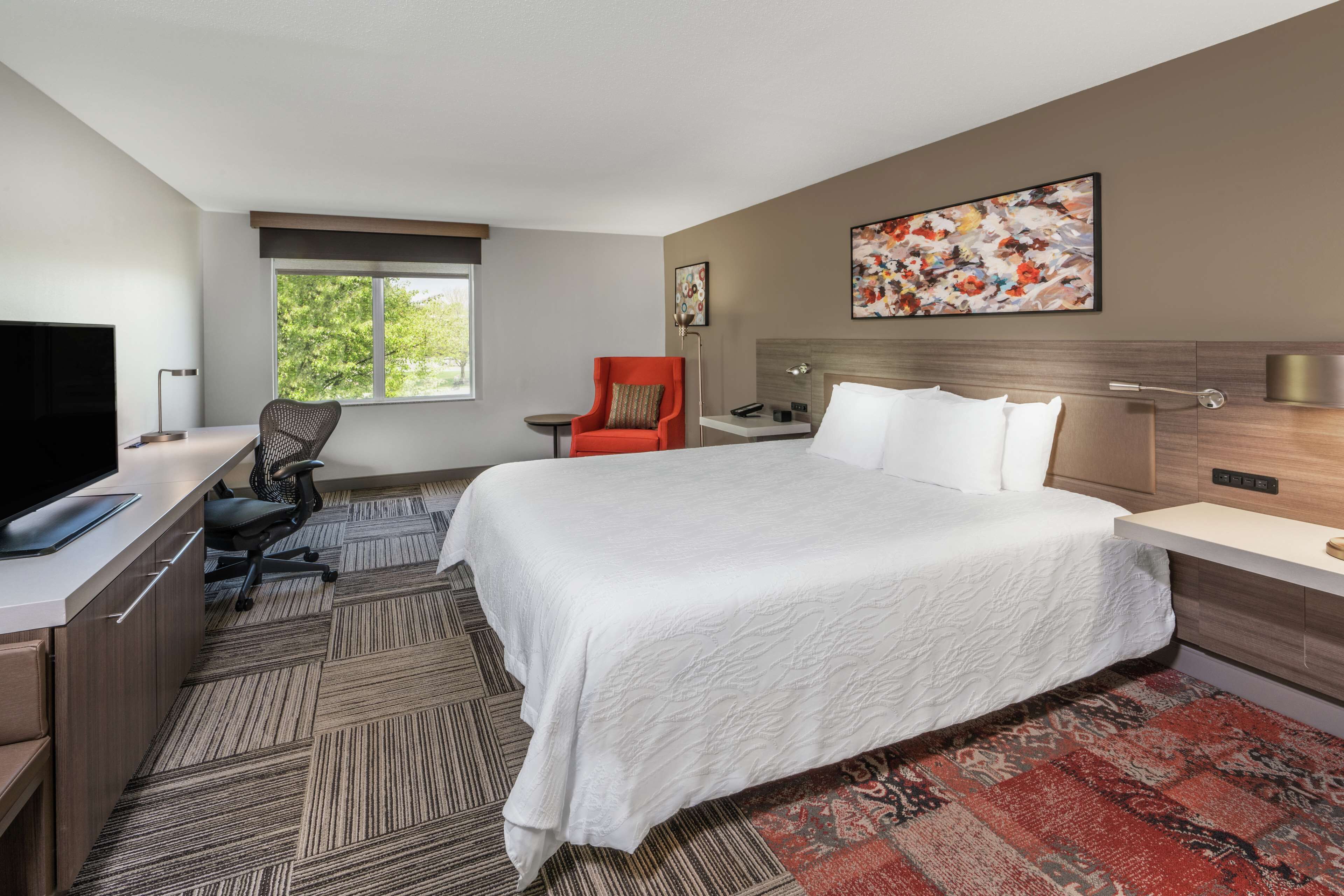 A hotel room with a bed, desk, chair, and a TV.