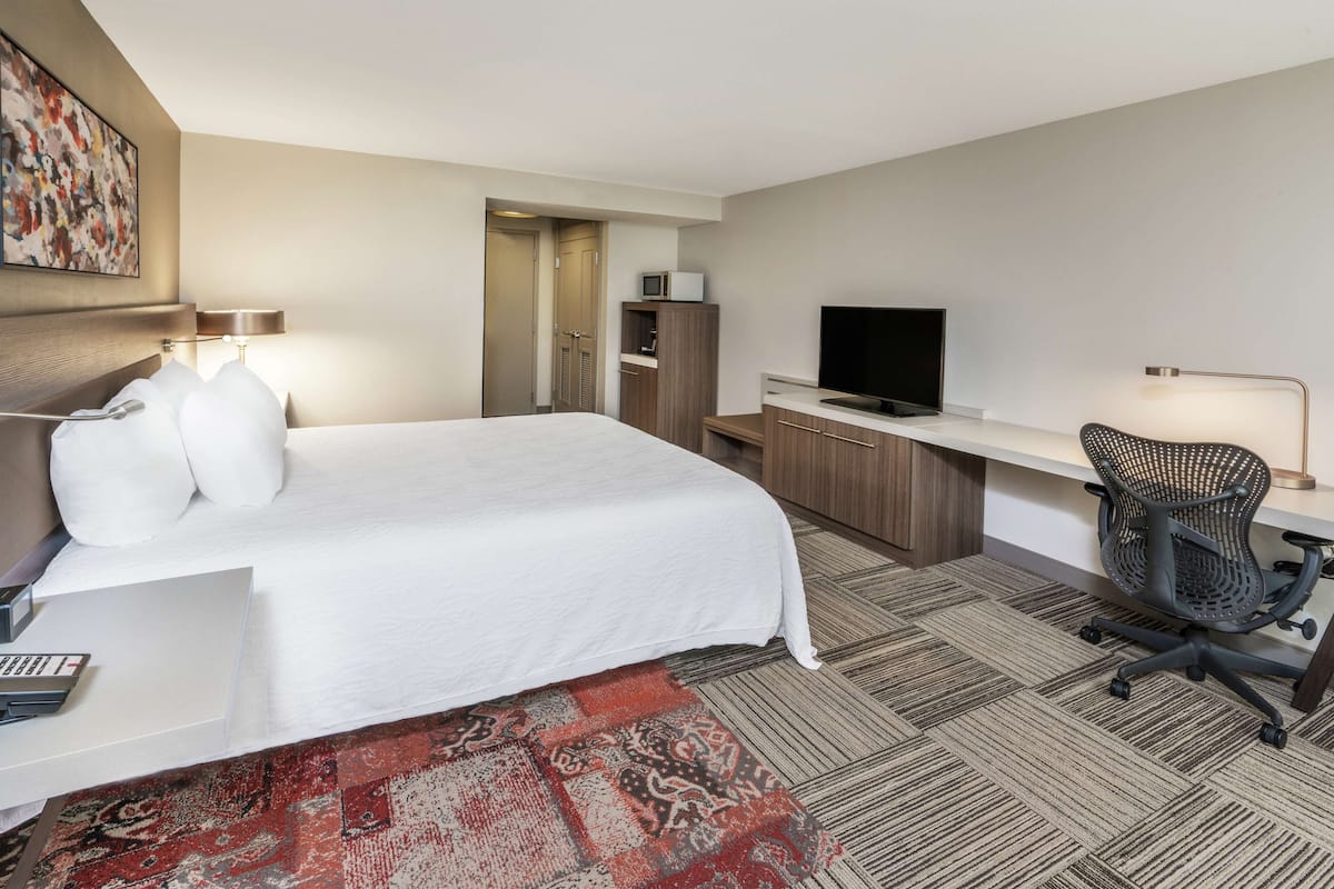 A hotel room with a large bed, a desk with a computer, a TV, and a chair.