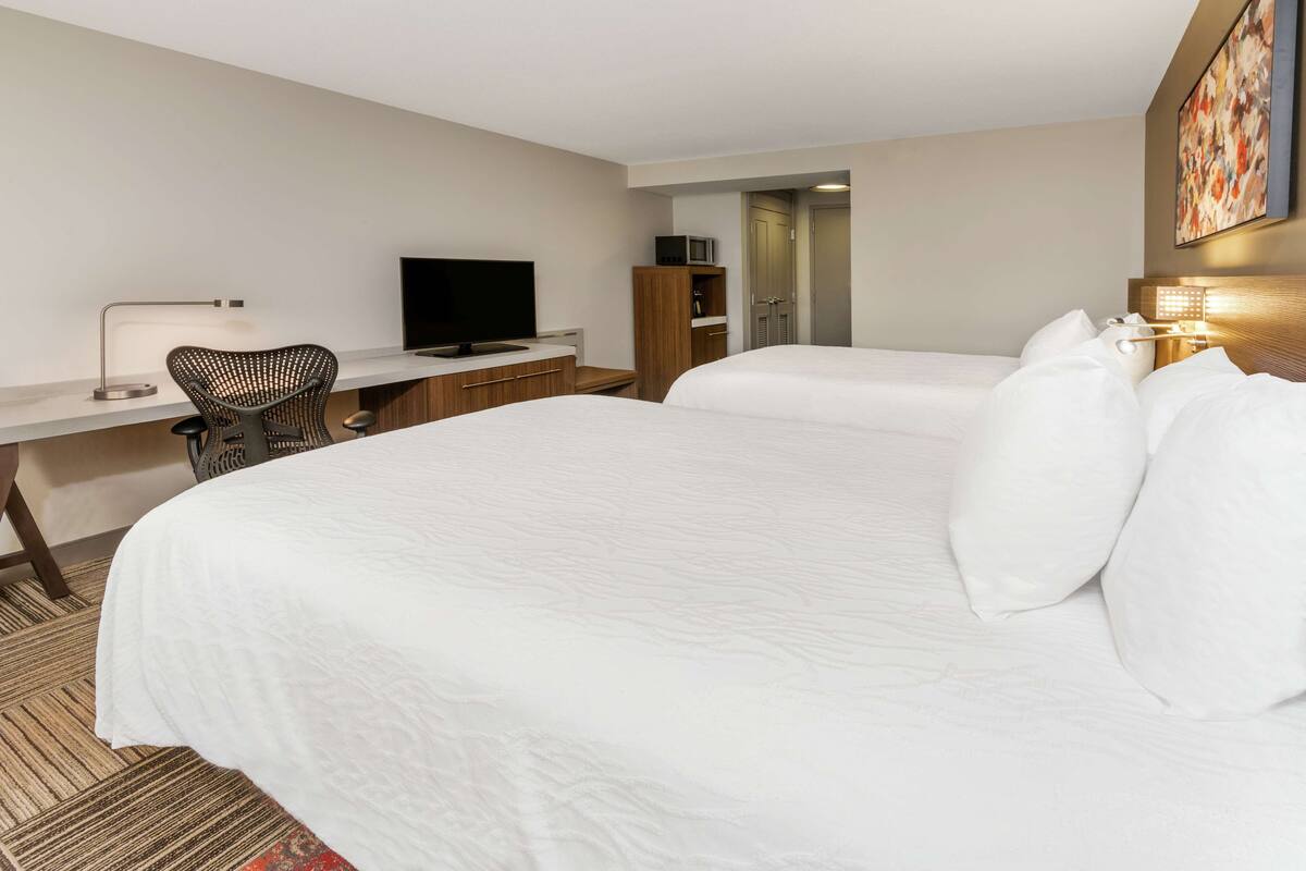 A hotel room with a large bed, a desk with a chair, a television, and a wardrobe.
