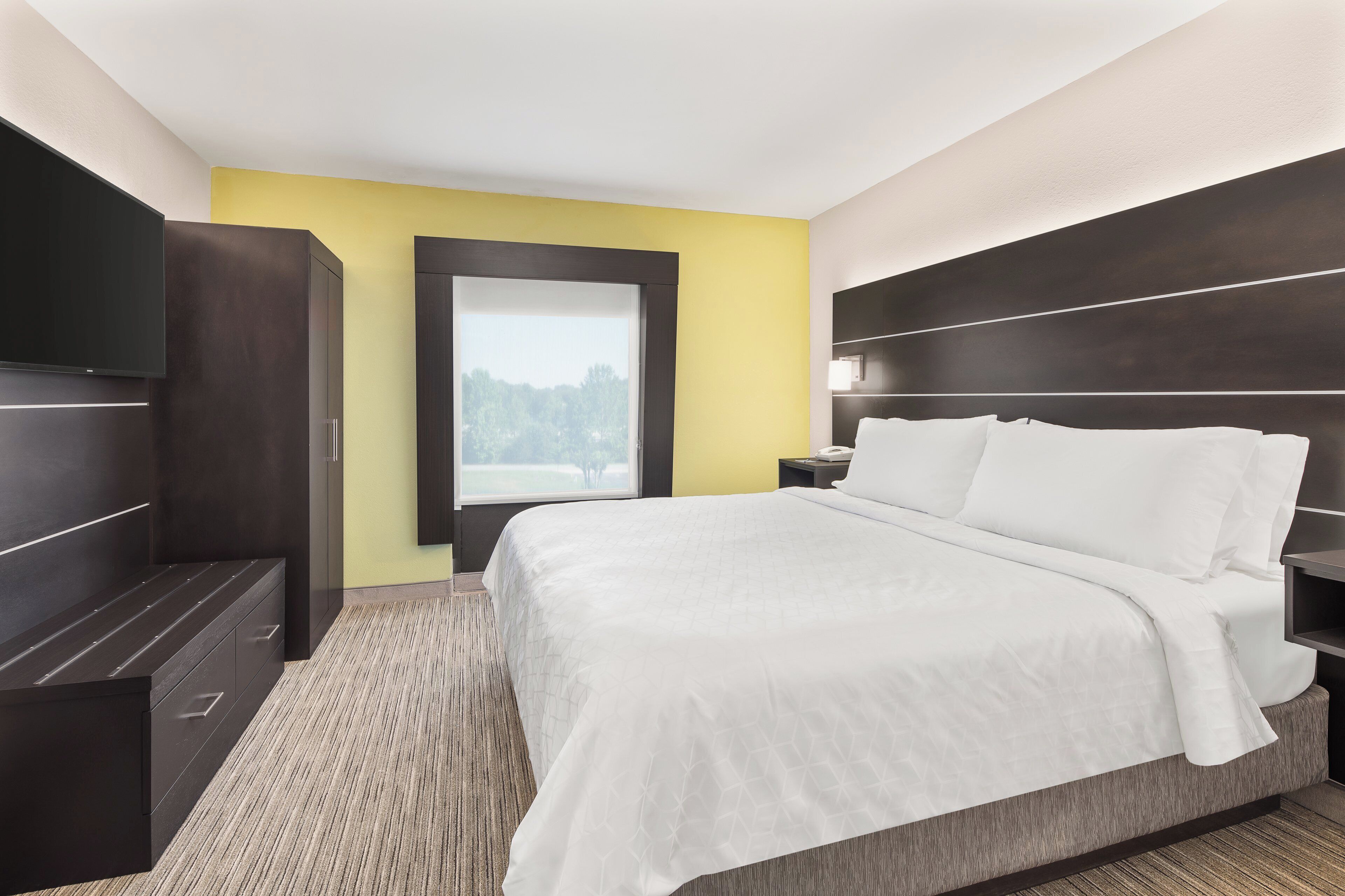 A hotel room with a bed, a nightstand, a wardrobe, and a window with a view of trees.