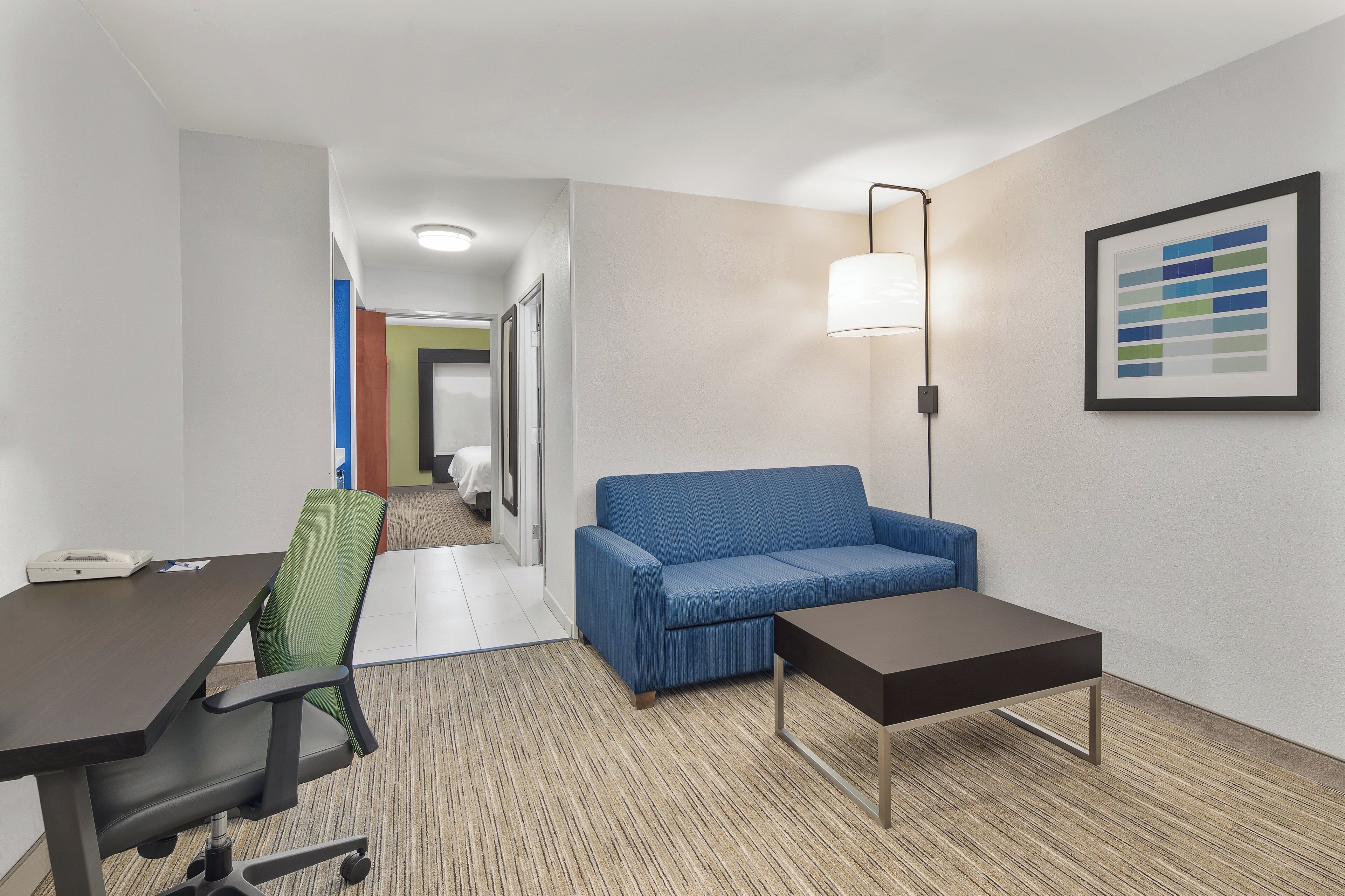 A hotel room with a desk, office chair, blue sofa, and a small table.