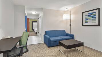 A hotel room with a desk, office chair, blue sofa, and a small table.