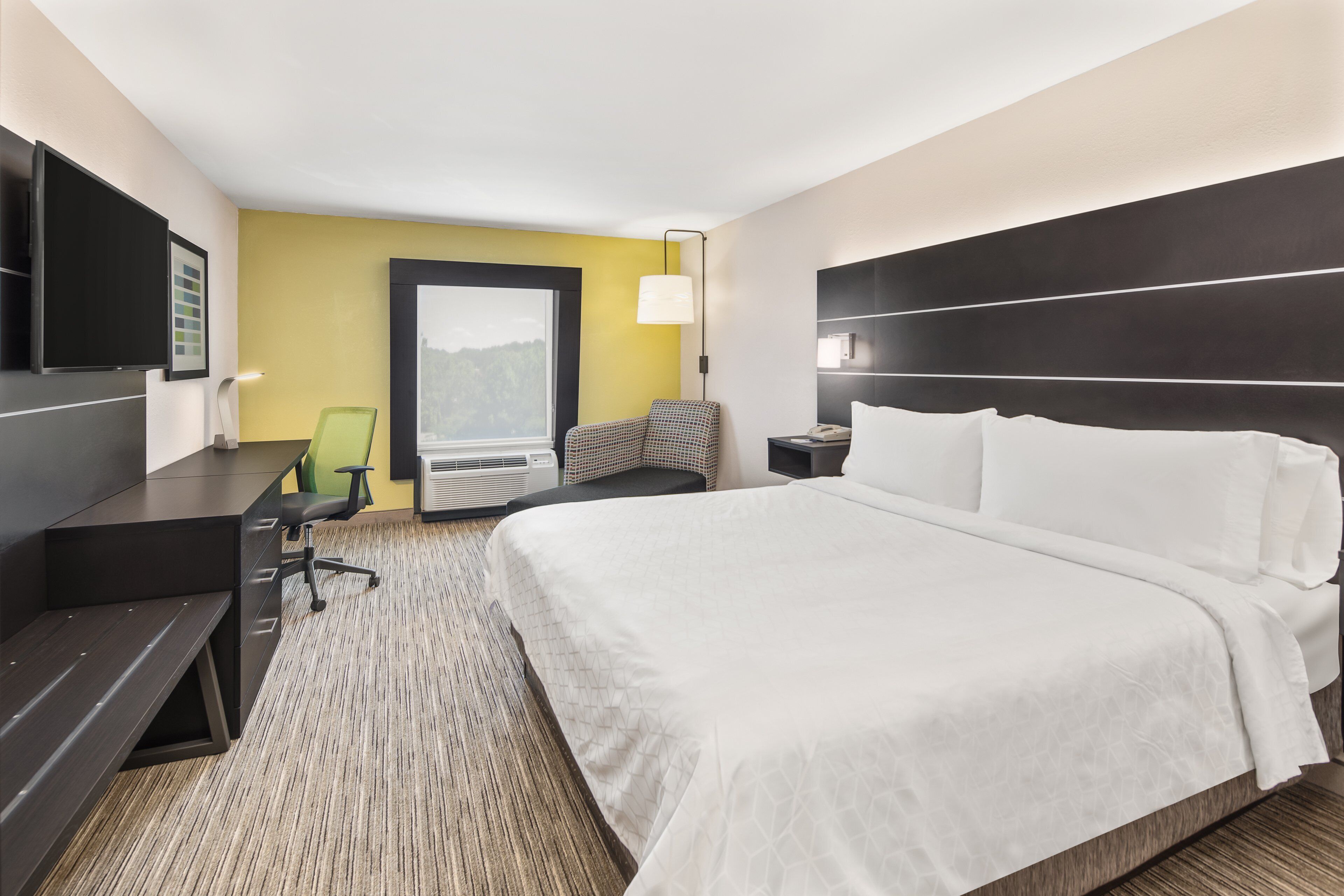 A hotel room with a large bed, a desk, a chair, a TV, and a window with a view.