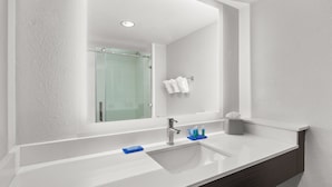 Une salle de bain moderne avec un grand miroir, un lavabo blanc et une douche à parois de verre.