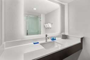 Un baño moderno con un espejo grande, un lavabo blanco y una cabina de ducha de vidrio.