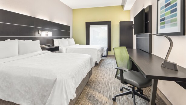 Une chambre d’hôtel avec deux lits, un bureau, une chaise, une télévision et une fenêtre.