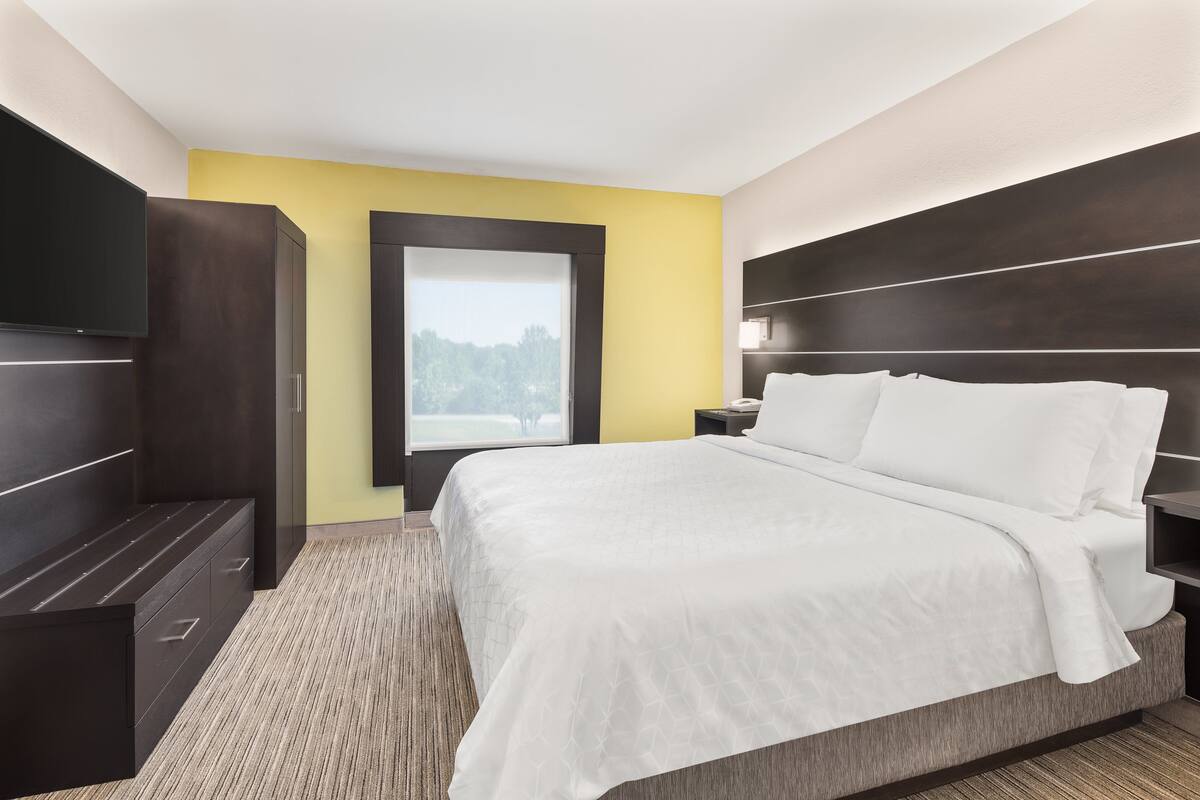 A modern hotel room with a large bed, built-in wardrobe, and a window with a view of trees.