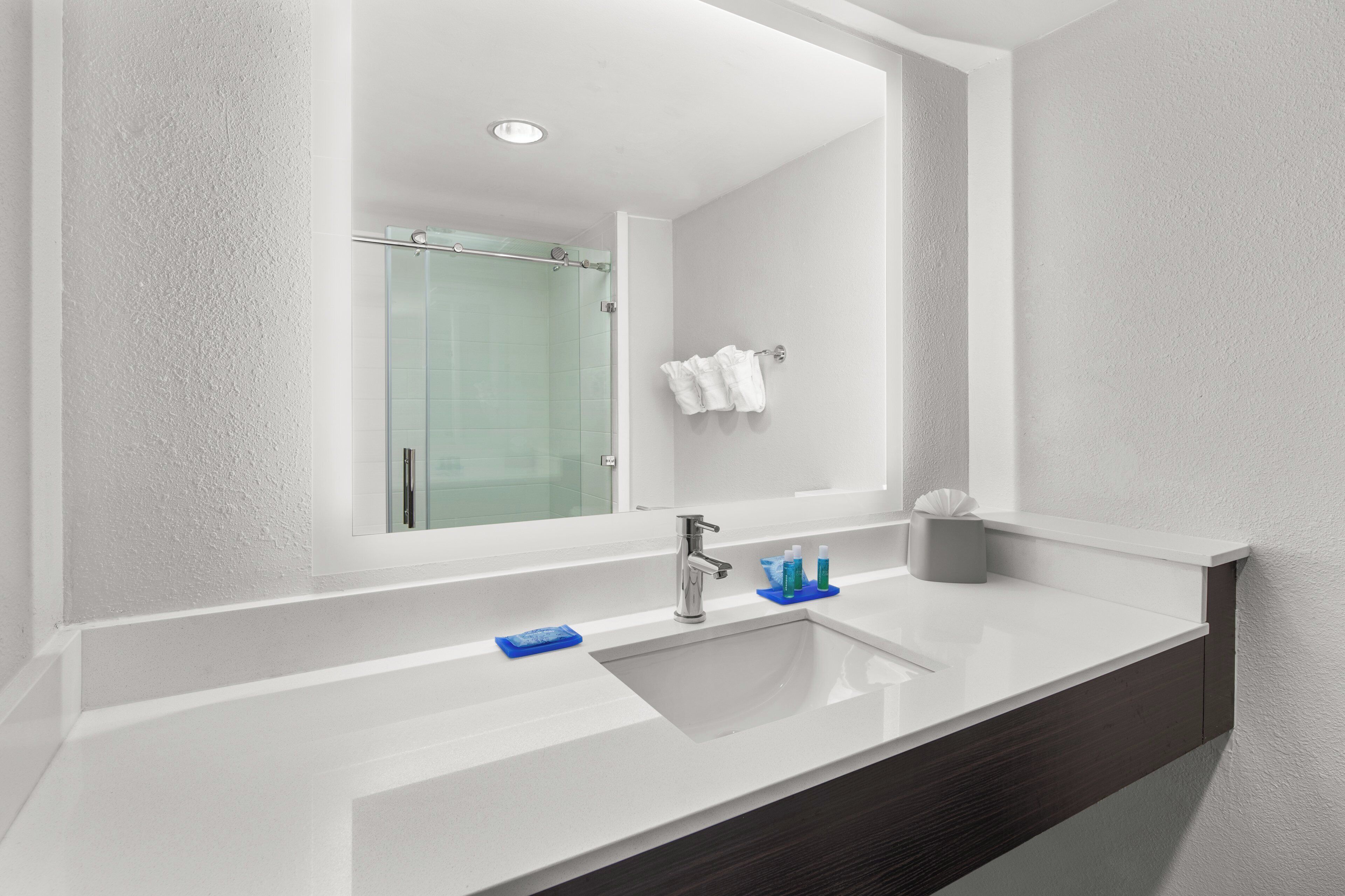 A modern bathroom with a large mirror, a sink, and a shower visible in the background.
