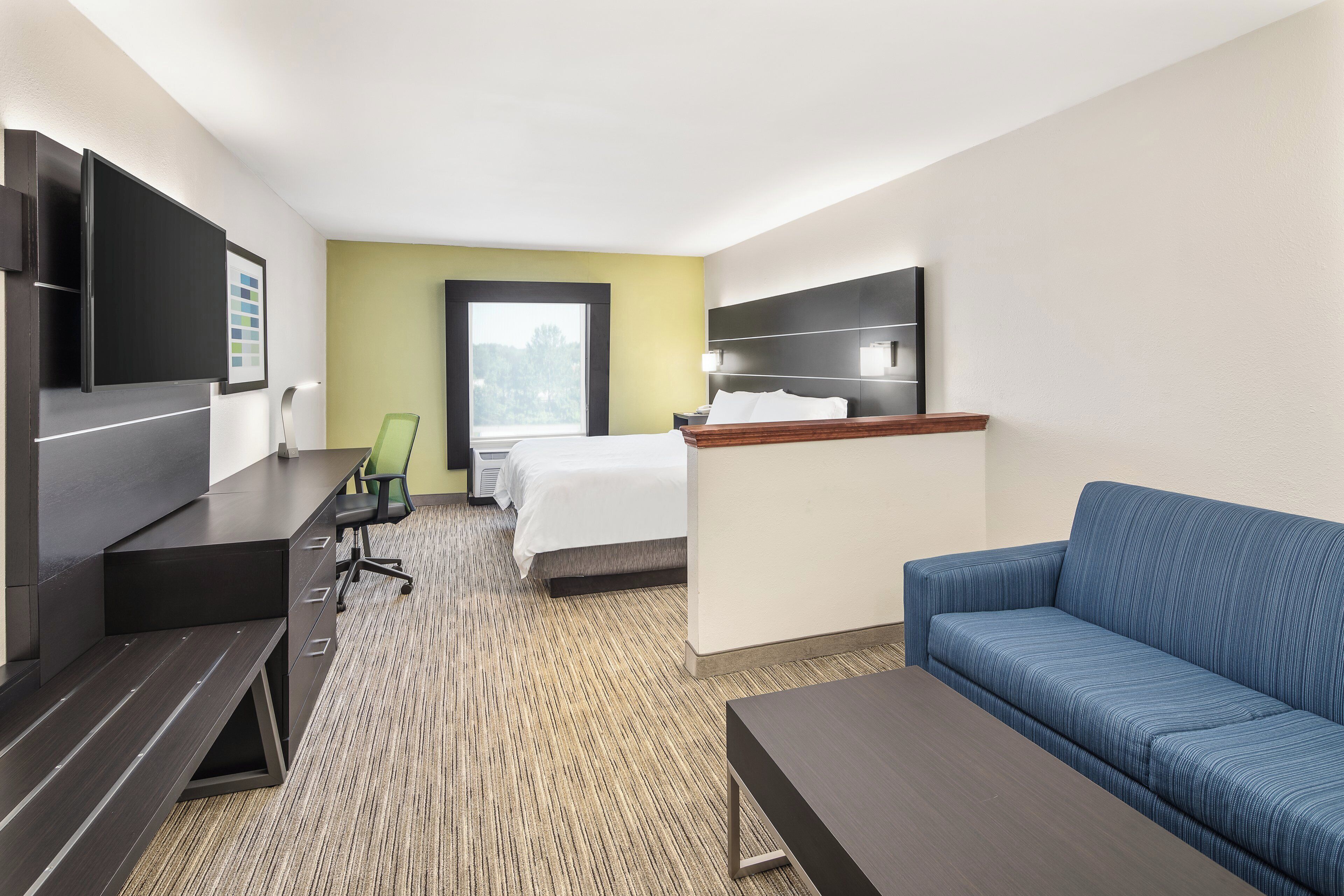 Habitación de hotel con cama, escritorio, televisor, sofá y ventana.