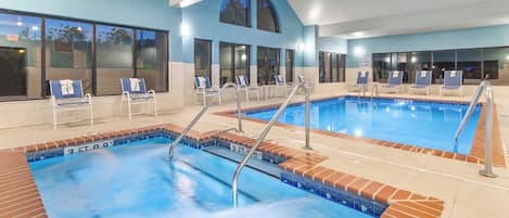 An indoor swimming pool with multiple lanes, lounge chairs, and a clear view of the sky through large windows.